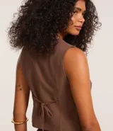 Chaleco corto color marrón, de corte sastre, con escote en V, doble botonadura y lazo en la espalda.