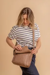 Bandolera de hombro color gris claro, con solapa frontal y correa ajustable. Presenta un diseño simple y práctico, ideal para uso diario.