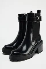 Botín negro estilo Chelsea con elástico lateral, hebilla decorativa y suela track con tacón bloque.