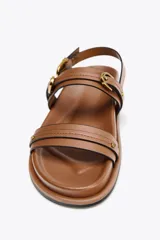 Sandalia plana color marrón con doble tira delantera con detalle de hebilla, punta redonda y pulsera al tobillo con cierre de hebilla.
