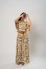 Vestido largo con estampado animal print en tonos camel, blanco y negro. Tiene escote en V, mangas cortas tipo murciélago y tajo frontal. Incluye cinturón ancho de cuero color camel.