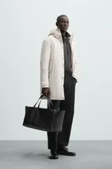 Parka color crudo de tejido técnico acolchado, con cuello alto y capucha ajustable. Tiene mangas largas con puños ajustables, bolsillos frontales con solapa, bolsillo interior y cierre frontal con cremallera oculta por solapa con botones a presión.