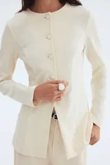 Blazer entallado color crema, de punto interlock pesado con cuello redondo y botones forrados hasta la cintura, creando un leve corte acampanado.