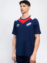 Remera de fútbol Umbro del Club Nacional de Football, modelo de entrenamiento. Diseño azul con detalles en blanco y rojo en cuello y mangas. Incluye logo de Umbro y escudo del club en el frente.
