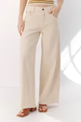 Pantalón de algodón color crema, de corte palazzo, tiro alto y ruedo desflecado. Incluye cinturón marrón con hebilla circular dorada.