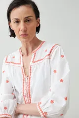 Blusa blanca de corte holgado con bordados de estrellas y detalles geométricos en color coral.
