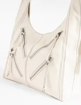 Cartera hobo color crudo de cuero sintético, con correa de hombro ajustable y múltiples cierres decorativos en el frente.