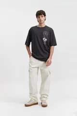 Pantalón cargo color beige, de corte recto, con bolsillos laterales y traseros. Se ajusta a la cintura con cinturón de cuero marrón.