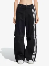 Pantalón de denim negro de corte ancho con tres tiras blancas verticales en los laterales y logo de Adidas.