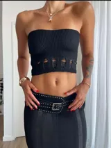 Conjunto de dos piezas negro compuesto por un top tipo bandeau y una falda larga de tejido de punto calado. El conjunto se complementa con un cinturón ancho de cuero negro con tachas metálicas y hebilla cuadrada.