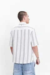 Camisa de manga corta con corte oversize, a rayas verticales blancas y grises, con cuello clásico y cierre frontal con botones. Confeccionada en algodón.