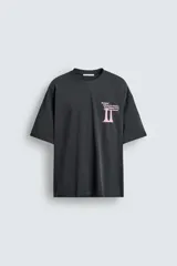 Camiseta negra de corte holgado con cuello redondo y mangas cortas. Estampado frontal y trasero con textos y figuras en color rosa.