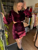 Conjunto de top corto y falda corta de terciopelo color borgoña. El top es de manga larga acampanada y cuello alto. La falda es drapeada y de tiro alto.