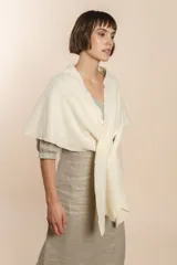 Chal asimétrico de lana color gris claro, con cortes en los hombros y doble ojal de fieltro para mantener el cruce. Terminación pespunteada y al corte.