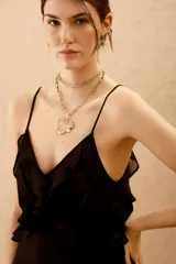 Vestido corto negro con escote en V, espalda descubierta y volados. Breteles finitos que se atan en la espalda con detalle de lurex. Ajuste elástico en la cintura.