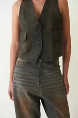 Chaleco marrón de denim con proceso de encuerado, escote en V, cierre frontal con botones y dos bolsillos con solapa y botón.
