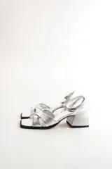 Sandalias plateadas de cuero, con tiras cruzadas sobre el empeine, pulsera al tobillo con hebilla y taco bajo cuadrado.