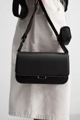 Bandolera negra con acabado grabado, compartimento principal con cierre mediante solapa imantada, bolsillo interior con cierre mediante cremallera, bolsillo frontal con cierre mediante cremallera, asa de hombro ajustable y monedero.