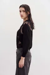 Sweater negro de punto con cuello redondo y mangas largas. Presenta recortes de encaje en la parte superior delantera y en los hombros.