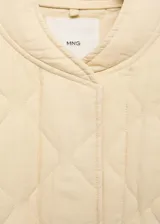 Chaqueta acolchada color crema, estilo bomber, con cuello perkins, cierre frontal con botones, dos bolsillos laterales y detalle fruncido en el bajo.