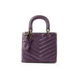 Cartera de mano color púrpura, con diseño acolchado en símil cuero soft y costuras a tono. Tiene acceso con cierre y broches imantados, herrajes dorados y correa regulable para usar como bandolera. El interior está forrado en tela de algodón y poliéster, con un bolsillo con cierre y dos abiertos.