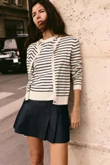 Chaqueta de punto color crema con rayas horizontales azul marino, cuello redondo, manga larga y cierre frontal con botones.