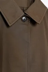 Trench color marrón con cuello solapa y manga tres cuartos. Tiene bolsillos delanteros y cierre frontal con cremallera y botones ocultos por solapa.