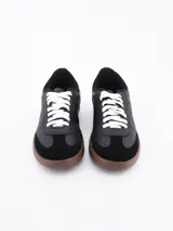 Zapatillas urbanas negras con cordones blancos y suela marrón.