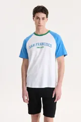 Remera blanca con mangas raglán celestes y cuello verde. Estampado frontal con la leyenda "San Francisco Since 1873" en celeste.