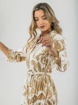 Vestido largo camisero con estampado floral en tonos beige y blanco, con cuello camisero, mangas 3/4 y falda escalonada. Incluye cinturón de soga con hebilla de madera.