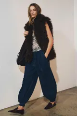 Pantalón bombacho de denim azul oscuro, tiro medio, con trabillas en la cintura, bolsillos delanteros y traseros, pespuntes marcados a contraste, bajo abullonado con puño y cierre frontal con cremallera, botón y ganchos metálicos.