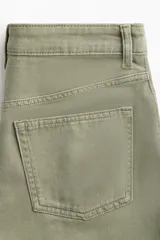 Pollera corta de denim color verde oliva, estilo cinco bolsillos, con cierre y botón frontal. Presenta apliques de tachas metálicas doradas y plateadas en forma de estrella o brújula distribuidas en el frente.