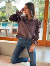 Camisa marrón de algodón con cuello clásico, cierre frontal con botones dorados, mangas largas abullonadas con puños elásticos y corte holgado.