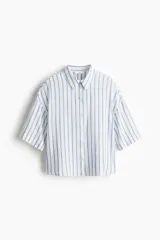 Camisa de corte holgado en tejido liviano de lino y viscosa, con cuello clásico, botones frontales, pliegue en la espalda, hombros caídos, mangas al codo y bajo redondeado. Diseño a rayas verticales azules y blancas.