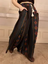 Pantalón palazzo marrón con bordados de estilo étnico en colores azul, naranja y rosa. Tiene cintura elástica con cordón ajustable y bolsillos laterales.