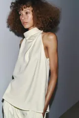 Top color crema, sin mangas, con cuello halter y cierre de botones en la nuca.