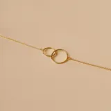 Pulsera de oro amarillo 18k con cadena fina y dos dijes circulares entrelazados.