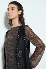 Chaleco largo color beige claro, estilo chaleco de gamuza, con apliques metálicos circulares perforados y largos flecos en el ruedo.