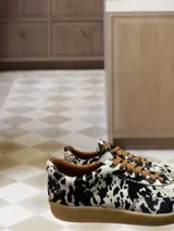 Zapatillas bajas con estampado animal print de vaca en blanco y negro, con cordones marrones y suela color caramelo.