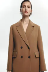 Abrigo largo color camel de Zara Woman Collection, confeccionado en hilatura con lana. Tiene cuello solapa con muescas, manga larga, falsos bolsillos delanteros, forro interior a contraste y cierre frontal con botones.