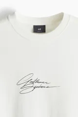 Remera blanca de corte holgado con estampado de texto en cursiva color negro en el centro del pecho.