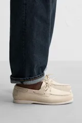 Zapato náutico color crema de cuero, con cordones alrededor del tobillo y suela plana.