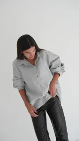 Camisa gris de lino con corte clásico, cuello camisero y mangas largas con puños abotonados.