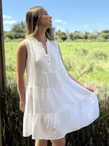 Vestido blanco de lino, sin mangas, con cuello mao y botones de nácar. Presenta varios cortes en su largo, aportando movimiento y un toque moderno a este diseño fresco y elegante.