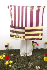 Pañuelo cuadrado de poliéster y elastano, de 1 metro x 1 metro, con estampado de franjas verticales en tonos bordó, blanco, lila y amarillo, y la palabra "CAPER" estampada en amarillo.