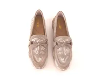 Mocasín de cuero gamuzado color avena, con bordados contrastantes, apliques metálicos y lazo decorativo en la capellada.