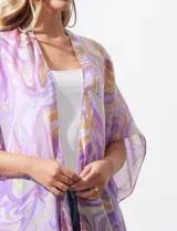 Kimono tejido con estampado abstracto en tonos verde, azul y blanco. Tiene mangas cortas amplias y terminación con borlas verdes en el ruedo.