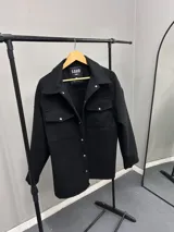 Chaqueta negra de paño con cuello clásico, cierre frontal con botones a presión, dos bolsillos de parche en el pecho y corte holgado.