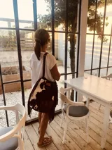 Cartera bandolera de cuero con estampado de vaca en blanco y marrón, con flecos de gamuza color chocolate en los laterales.