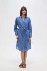 Vestido camisero de algodón color azul, de corte ancho y manga larga, con cuello camisero y lazo ajustable a la cintura.